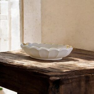Un plat ovale en céramique blanche, aux bords festonnés et rehaussés d'or, posé sur une table en bois brut.