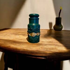 Pot avec couvercle vert bouteille avec une moulure et d’un liseré en feuille d’or posé sur une table en bois rustique