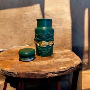 Pot avec couvercle vert bouteille avec une moulure et d’un liseré en feuille d’or posé sur une table en bois rustique