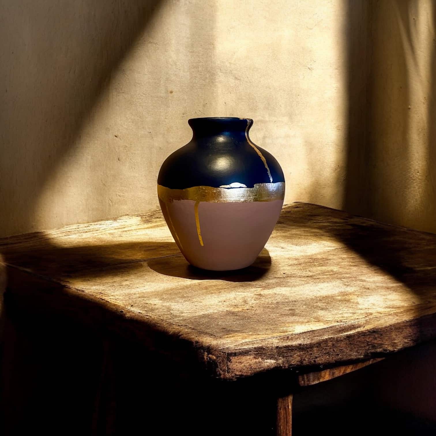 Vase rond rose poudré et bleu marine posé sur une table en bois rustique