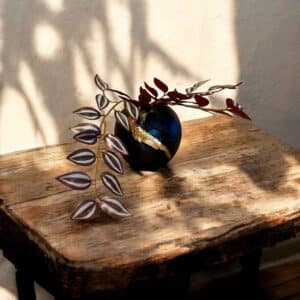 Vase rond noir avec une moulure oiseau et de la feuille d’or posé sur une table rustique, avec un bouquet