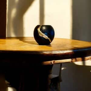 Vase rond noir avec une moulure oiseau et de la feuille d’or posé sur une table rustique