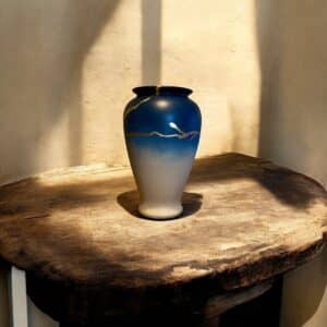 Vase dégradé bleu tirant sur ke beige avec un liseré fin en feuille d’or posé sur une table en bois rustique