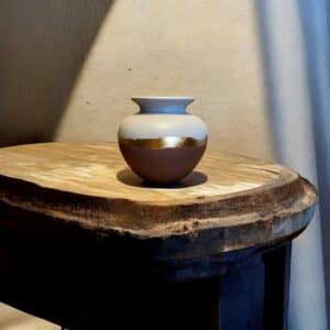 Vase rond rose et blanc avec un liseré en feuille d’or posé sur une table en bois rustique