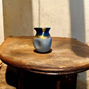 Petit vase bleu marine et gris avec un liseré d’or posé sur une table en bois rustique