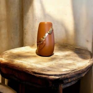 Vase Terracotta avec deux moulures oiseaux recouverts de feuille d’or posé sur une table en bois rustique