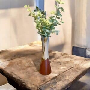 Grand vase beige et bordeaux avec un liseré en feuille d’or posé sur une table en bois rustique Avec un bouquet De branches d’eucalyptus