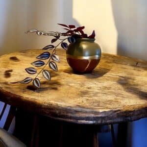 Vase rond kaki et bordeaux avec un liseré en feuille d’or posé sur une table en bois rustique, avec une plante dedans