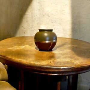 Vase rond kaki et bordeaux avec un liseré en feuille d’or posé sur une table en bois rustique