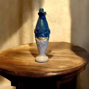 Vase haut et fin beige et bleu avec moulure et liseré en feuille d’or posé sur une table en bois rustique
