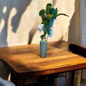 Petit vase gis bleu avec un liseré d’or posé sur une table en bois rustique, avec un petit bouquet