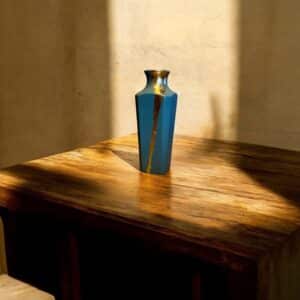 Petit vase gis bleu avec un liseré d’or posé sur une table en bois rustique