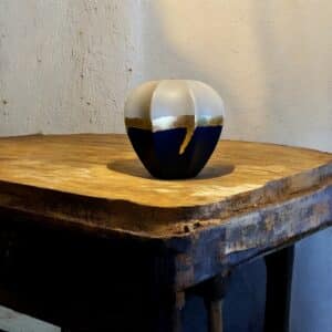 Vase beige et bleu marine avec un liseré feuille d’or posé sur une table en bois rustique