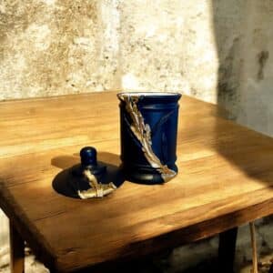 Pot avec couvercle bleu marine avec des moulures et de la feuille d’or posé sur une table en bois rustique