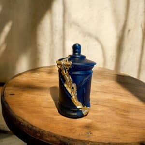 Pot avec couvercle bleu marine avec des moulures et de la feuille d’or posé sur une table en bois rustique
