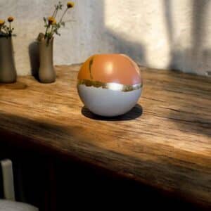 Vase rond beige et terracotta avec un liseré en feuille d’or posé sur une table en bois rustique