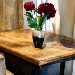 Grand vase noir et beige avec un liseré en feuille d’or posée sur une table en bois rustique, avec des fleurs rouges