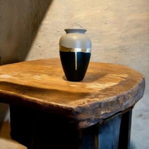 Grand vase noir et beige avec un liseré en feuille d’or posée sur une table en bois rustique