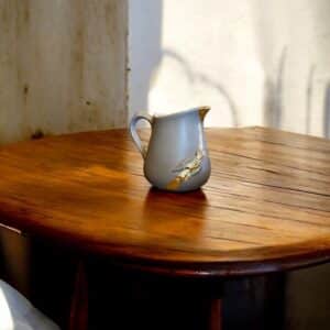 Petit pichet beige avec moulure oiseaux et feuille d’or posé sur une table en bois rustique