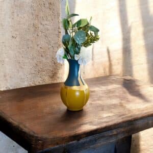 Vase jaune moutarde et bleu avec un liseré en feuille d’or avec un bouquet de fleurs blanches posé sur une table en bois rustique