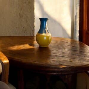 Vase jaune moutarde et bleu avec un liseré en feuille d’or posé sur une table en bois rustique