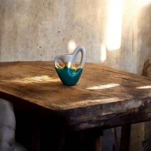 Petit vase gris et vert avec un liseré en feuille d’or, avec deux anses, posé sur une table en bois rustique