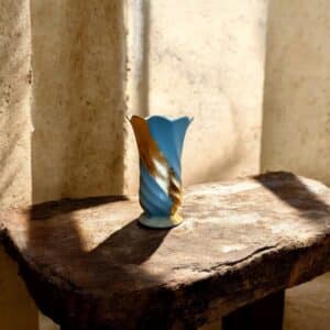 Petit vase gris bleu torsadé avec un liseré en feuille d’or posé sur une table en bois rustique