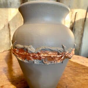 Vase en terre cuite relooké en beige avec une moulure et de la feuille d’or couleur bronze, posé sur une table rustique