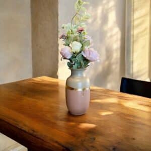 Grand vase beige et rose poudré avec un liseré en feuille d’or posé sur une table en bois rustique, avec un bouquet de fleurs blanches et roses