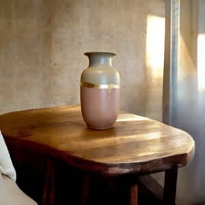 Grand vase beige et rose poudré avec un liseré en feuille d’or posé sur une table en bois rustique