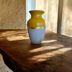 Grand vase jaune et gris avec un liseré en feuille d’or posé sur une table en bois rustique