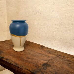vase bleu et blanc avec un liseré en feuille d'or posé sur une table rustique en bois